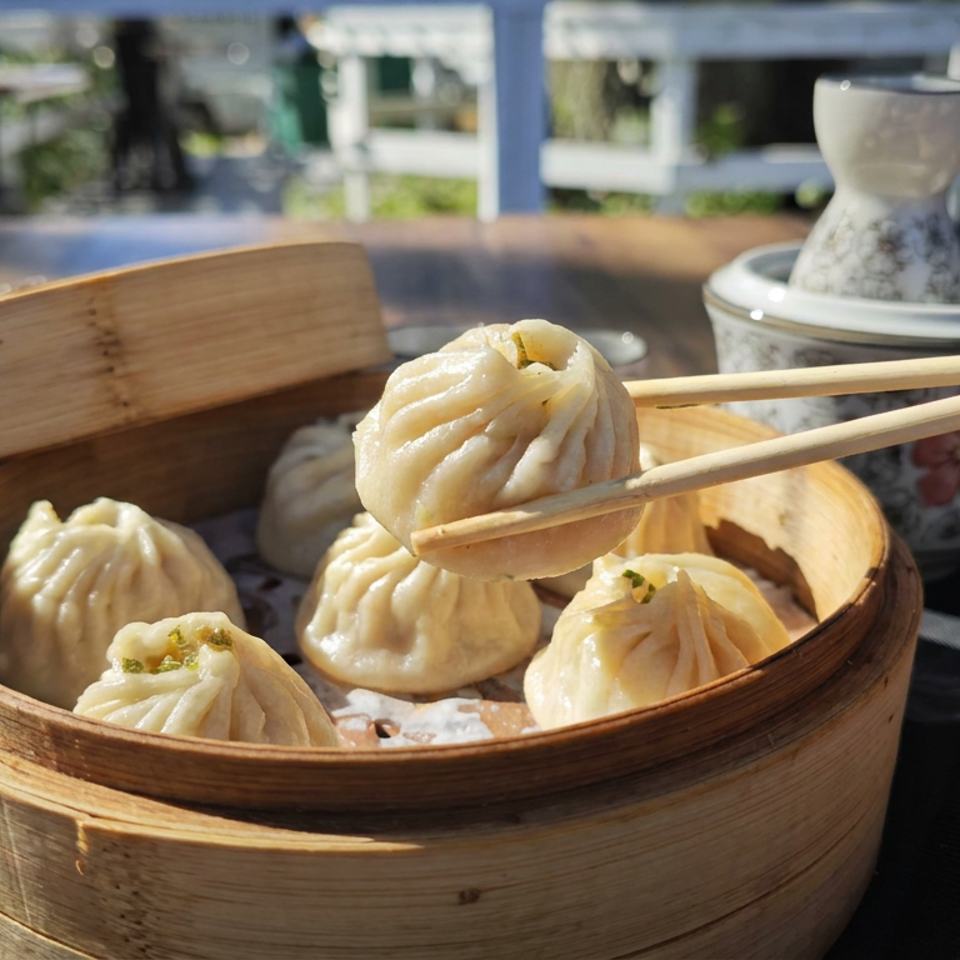 Chopsticks lift a steamed dumpling from a bamboo basket of dumplings on an outdoor dining table.