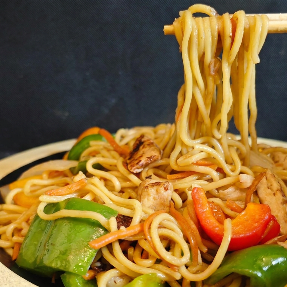 Stir-fried noodles with chicken and colorful bell peppers on a plate, with chopsticks lifting noodles.
