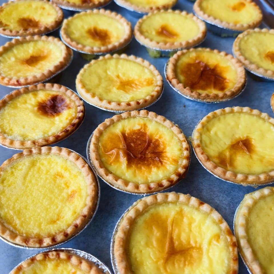 Tray of golden custard tarts with flaky crimped crusts, some topped with caramelized brown spots.