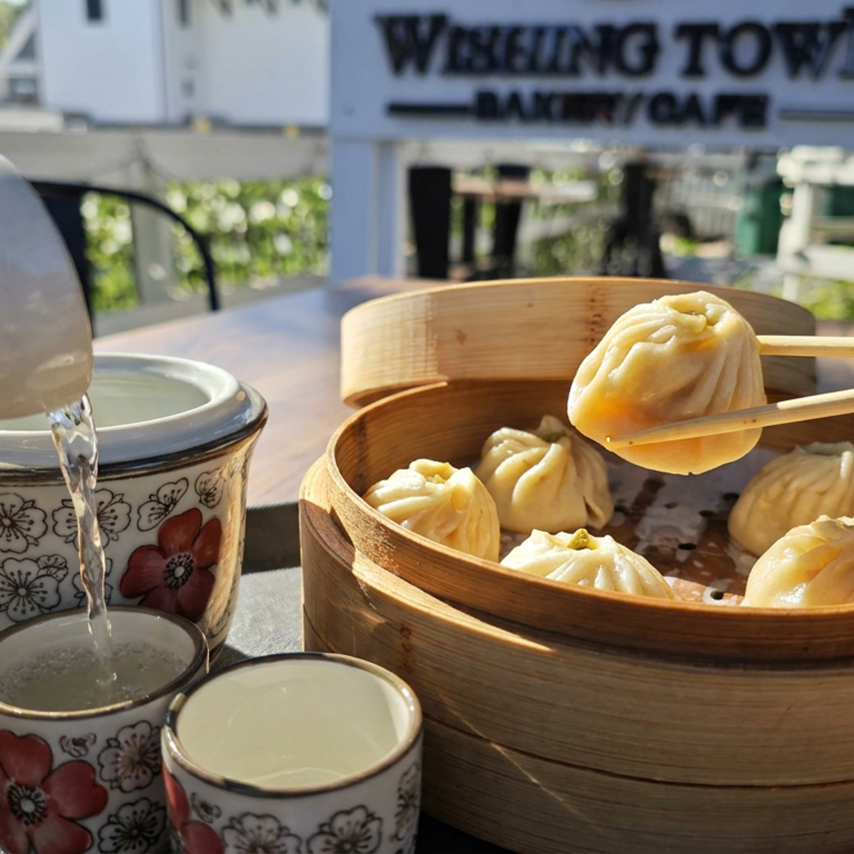 Steaming dumplings in a bamboo basket with chopsticks, floral teacups, and pouring tea at Winking Town Bakery Cafe.